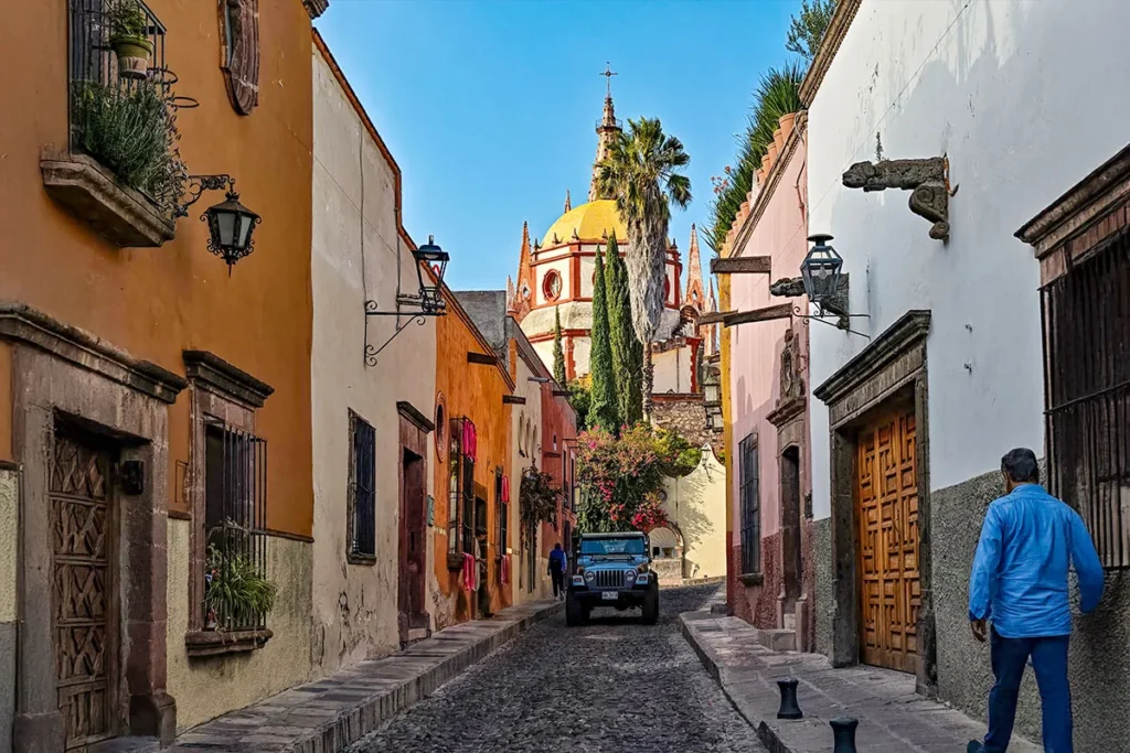 Cobblestone street in Centro, San Miguel de Allende, with colorful colonial houses and a view of the Parroquia in the distance.
