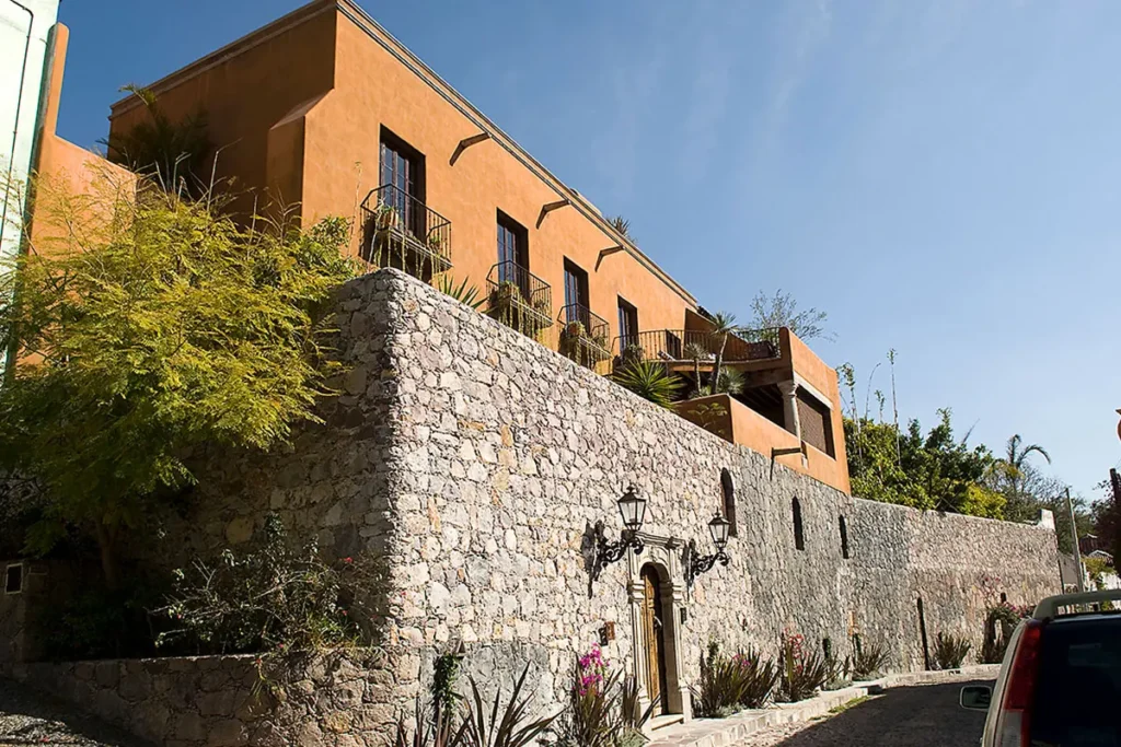 Colonial-style home in San Miguel de Allende’s Atascadero neighborhood, featuring a stone façade, wrought-iron balconies, and warm terracotta walls under clear blue skies.