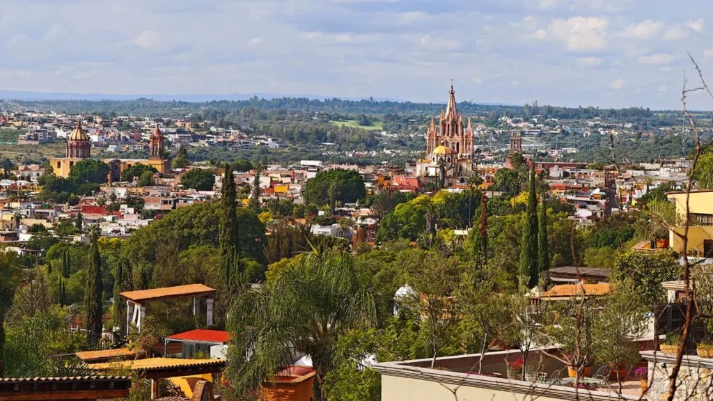 Panoramic view of San Miguel de Allende from Atascadero, showing hillside homes, greenery and the city skyline in the background.