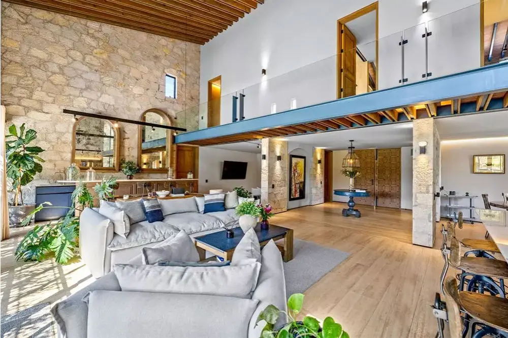 Open-plan living room with gray sectional sofas, a stone feature wall, and a mezzanine balcony above the seating area.