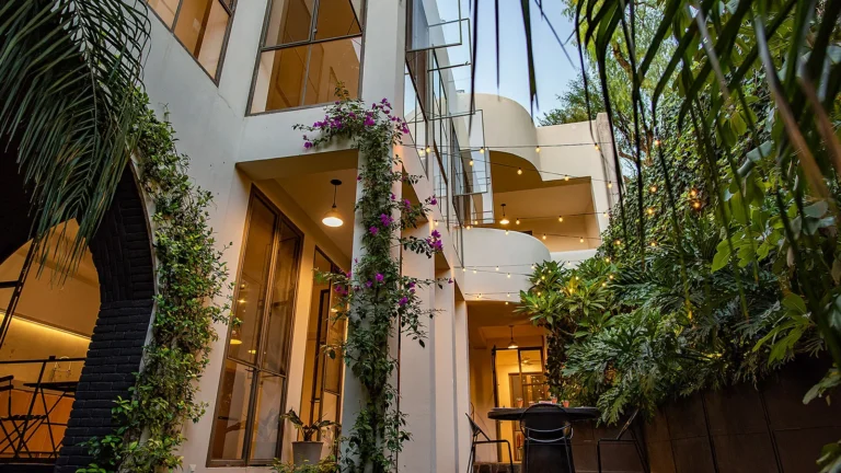 Hidden-Costs-of-Buying-Luxury-Property-in-San-Miguel-de-Allende - Colonial Real Estate - Colonial Real Estate Modern luxury home courtyard in San Miguel de Allende with bougainvillea, lush gardens, and string lights, illustrating the ownership costs of high-end properties in the city.